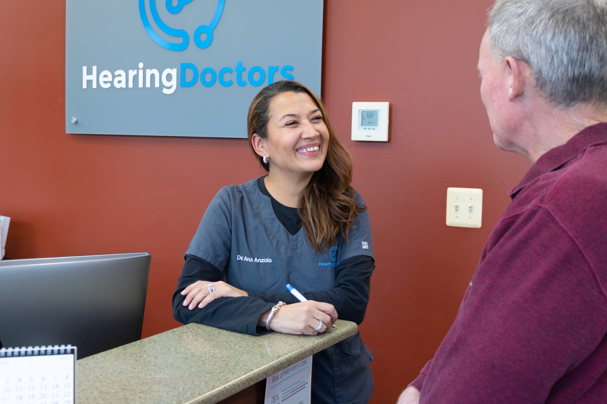 A audiologist smiles while engaging in conversation with a man at a welcoming office desk.
